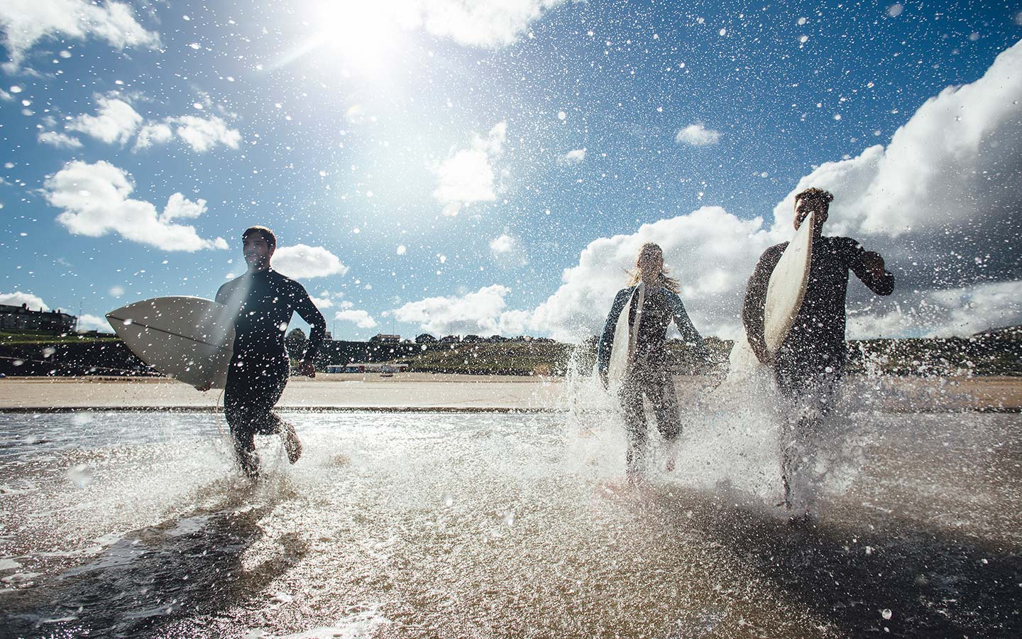 3 people with surfboards running in the water