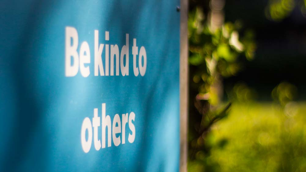 Be kind to others sign with green leaves and grass in the background
