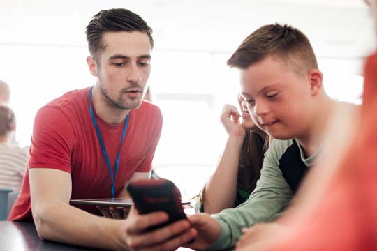 A teacher and a pupil with Down's Syndrome engage on a task that uses a mobile phone