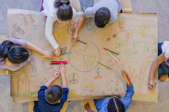 Children drawing together on a massive sheet of brown wrapping paper