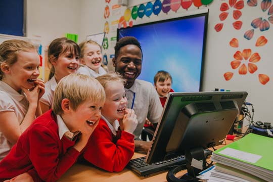 Happy teacher and children laugh as they watch something on the computer screen