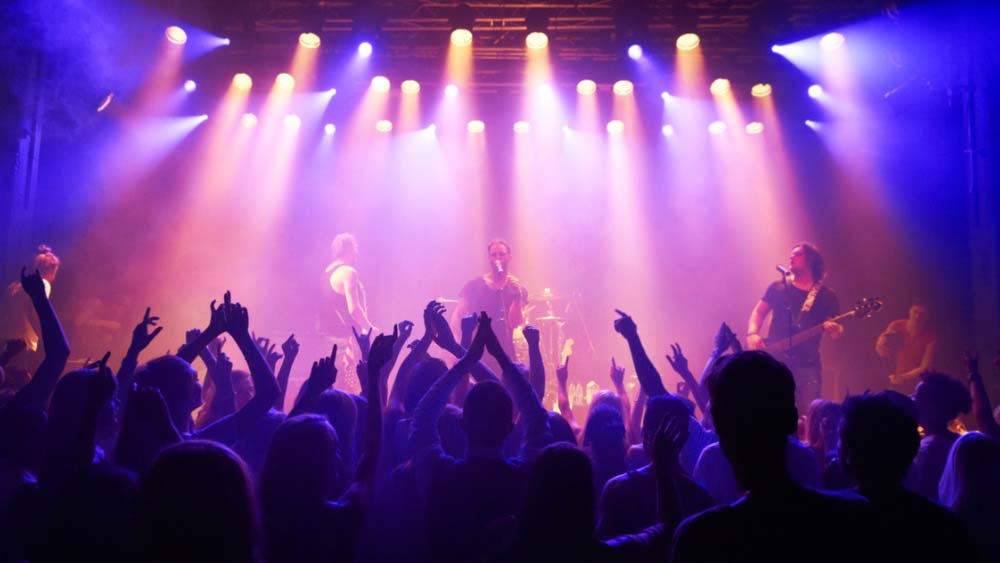Band on stage in coloured lights, fans hands in the air