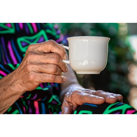 An elderly person's hands clasping a mug