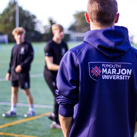 A student wearing a Marjon branded hoodie on a sports pitch