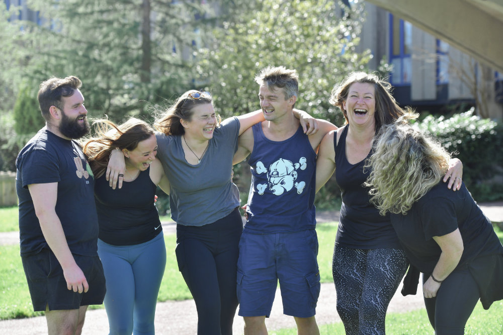 Five students standing arm in arm in the Marjon quad and laughing